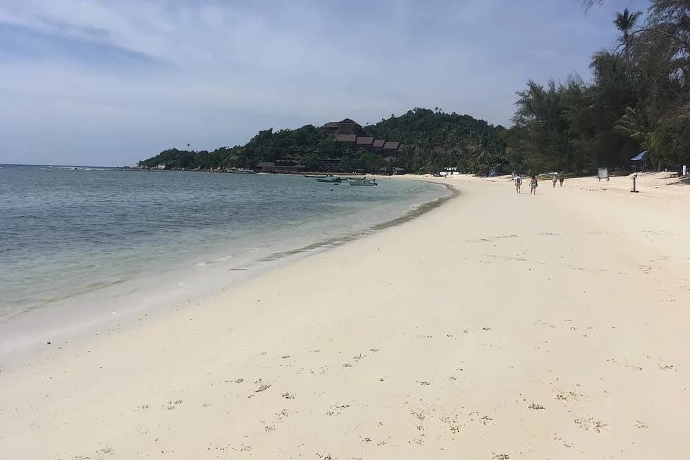 The long white sand curve of Haad Yao with a forested headland at the far end.