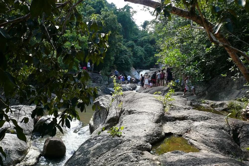Smooth granite slabs and shallow pools at Pho Darng waterfall, with jungle closing in overhead.