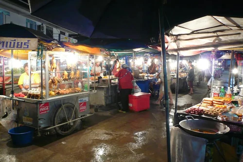 Food carts and vendors under awnings at the Thong Sala night market after dark.