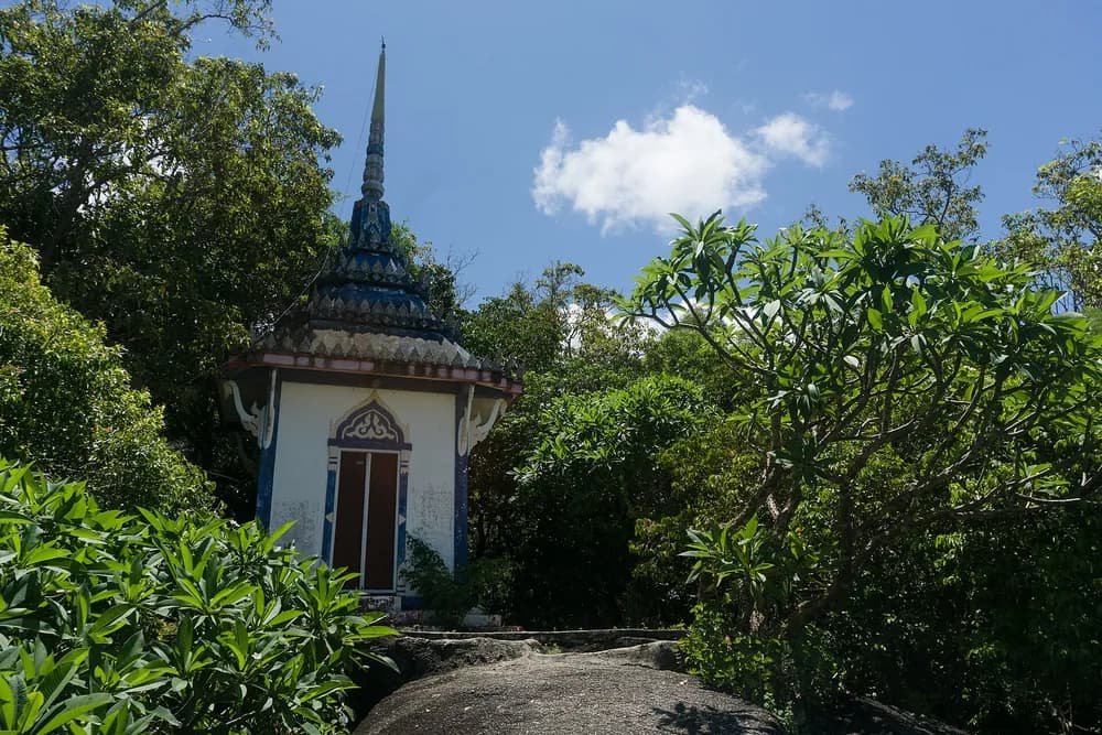The white chedi and blue-tiled spire of Wat Khao Tham rising out of the hillside jungle.