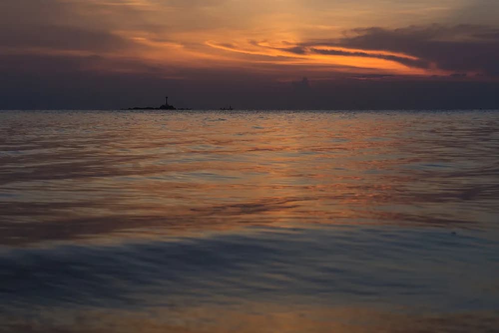 Sunset over the Gulf of Thailand from Zen Beach, the sky banded orange above still water.